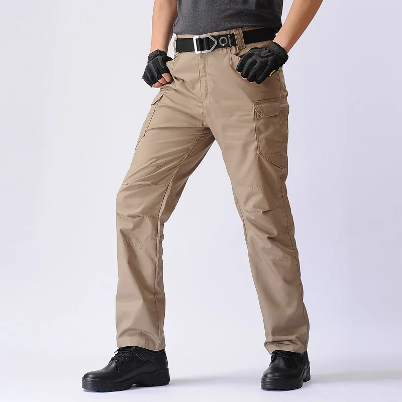 Vêtue du Pantalon tactique multifonctionnel résistant et confortable dOlivias Boutique, dun pantalon cargo beige, dun t-shirt foncé, de gants noirs, dune ceinture et de chaussures noires, la personne se tient sur un fond blanc uni.