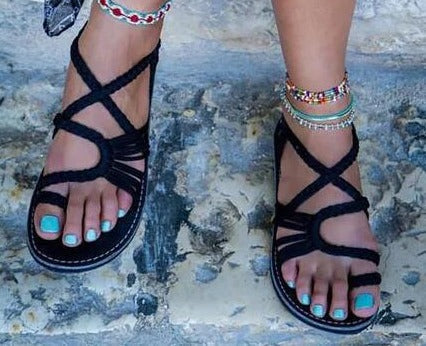 Une personne se tient debout sur une surface en pierre texturée, reflétant le style estival dans les Sandales de Plage Colorées d'Olivia Boutique. Les sandales à lanières noires avec des ongles peints en turquoise et des bracelets de cheville à perles colorées promettent un confort exceptionnel pour toute aventure en bord de mer.