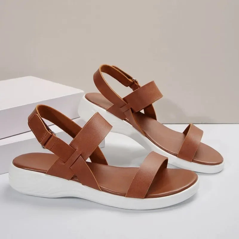 Les sandales d'été orthopédiques d'Olivia's Boutique, dotées d'un design à lanières marron et de semelles coussinées blanches, sont présentées sur une surface claire. Une sandale repose sur une boîte blanche, mettant en valeur son bout ouvert et sa bride à la cheville pour une durabilité et un soutien optimal.