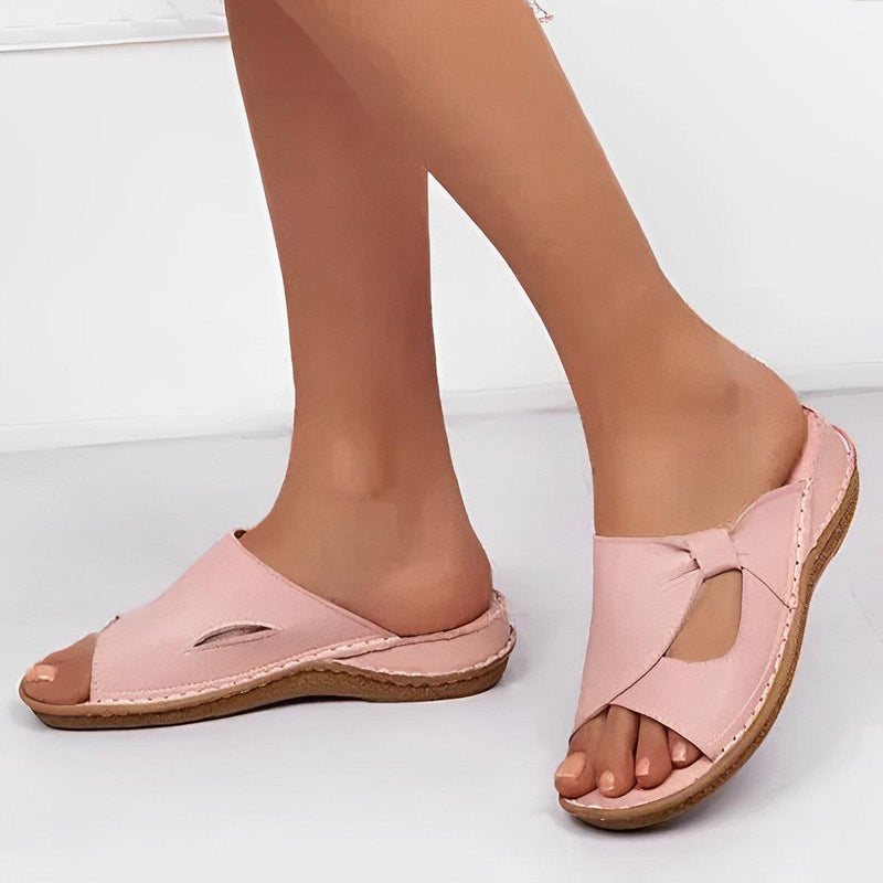 Une personne portant les Sandales en Cuir PU Confortables ARLA d'Olivia's Boutique, rose clair avec un design de nœud découpé et une semelle beige de soutien, sur un fond blanc uni.