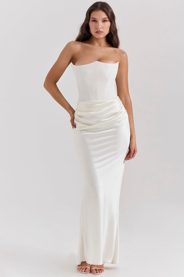 Dans une scène captivante, elle porte la Robe Corset à Lacets Emilia dOlivias Boutique, mettant en valeur son design en satin sans bretelles. Ses longs cheveux ondulés flottent magnifiquement tandis quelle porte un maquillage minimaliste, prenant une pose gracieuse avec les mains sur les hanches.